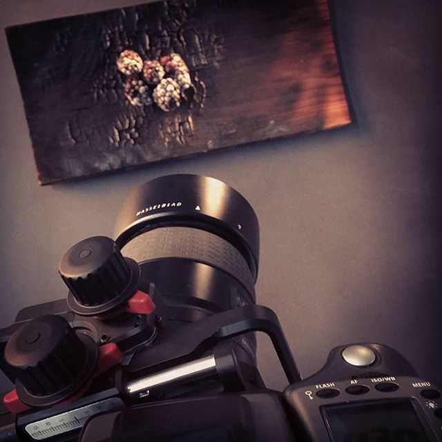 A professional Hasselblad camera on a tripod points towards a wooden board art piece in a studio setup.