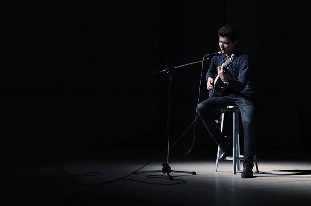 A musician plays guitar on stage under the spotlight.