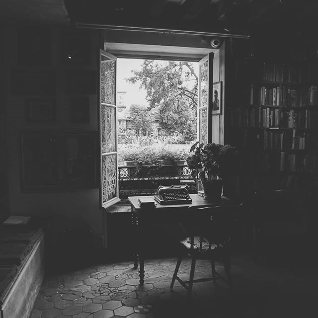 A vintage typewriter sits on a desk by an open window in a cozy room with bookshelves.
