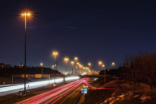 A long exposure shot captures light trails on a highway at night, lit by streetlights against a dark sky.