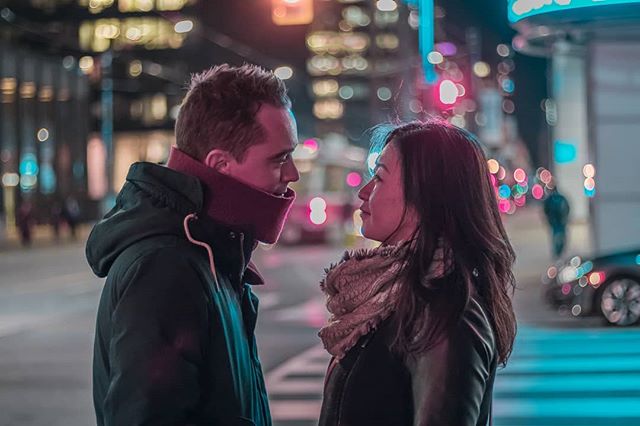 A couple shares an intimate moment on a city street at night, with a shallow depth of field and bokeh.