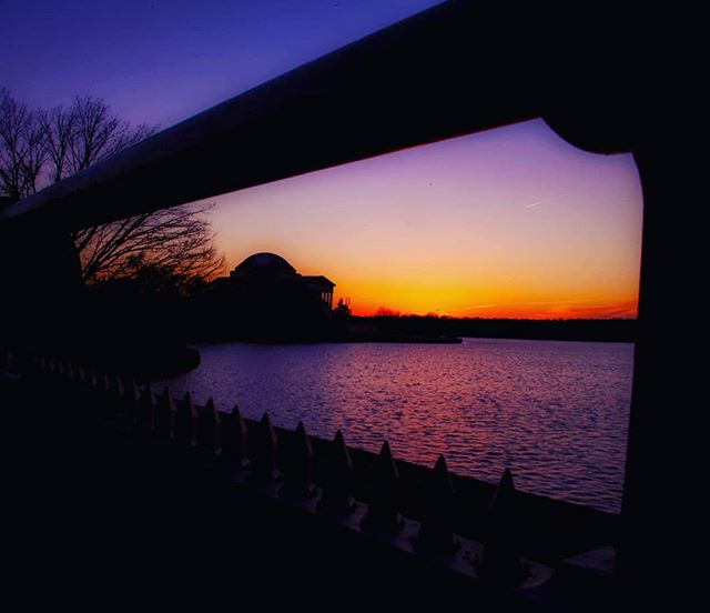Sunset over the Jefferson Memorial reflected in the water, framed by architectural details.